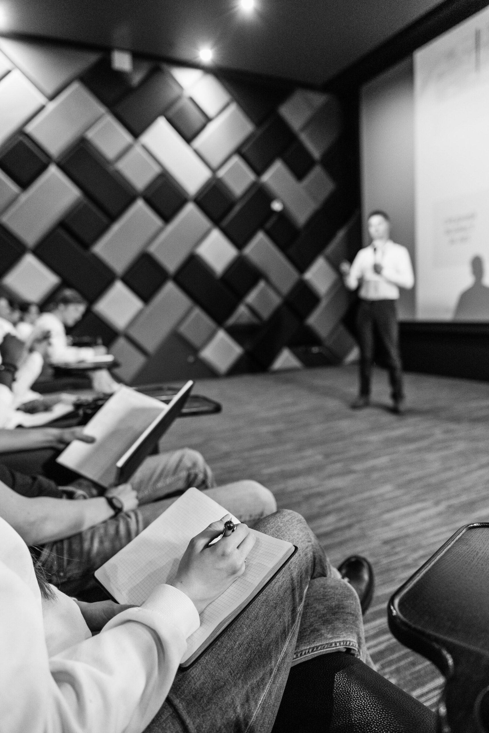 Black and white shot of students taking notes during a lecture in a modern hall.